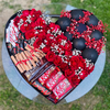 Heart-shaped arrangement with red roses, black ornaments, and candy bars on a grassy background