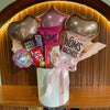 Gourmet gift basket with candy bars and balloons on a wooden surface