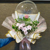 Bouquet of flowers in a transparent bubble with decorative ribbons, held by a person wearing a blue glove.