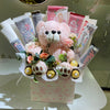 Bouquet with a pink teddy bear, flowers, and chocolate bars on a white surface.