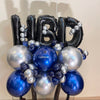 Balloon arrangement with 'HBD' letters and blue, silver, and black balloons on a neutral background.