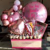 Gourmet gift basket with balloons, candy bars, and confetti on a table.