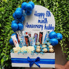 Gift basket with candies, flowers, and balloons with 'Happy 6th month Anniversary hubby' text against a green leafy background.
