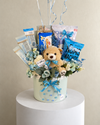 Close-up of the pastel blue birthday gift basket with a teddy bear, chocolates, snacks and a blue ribbon.