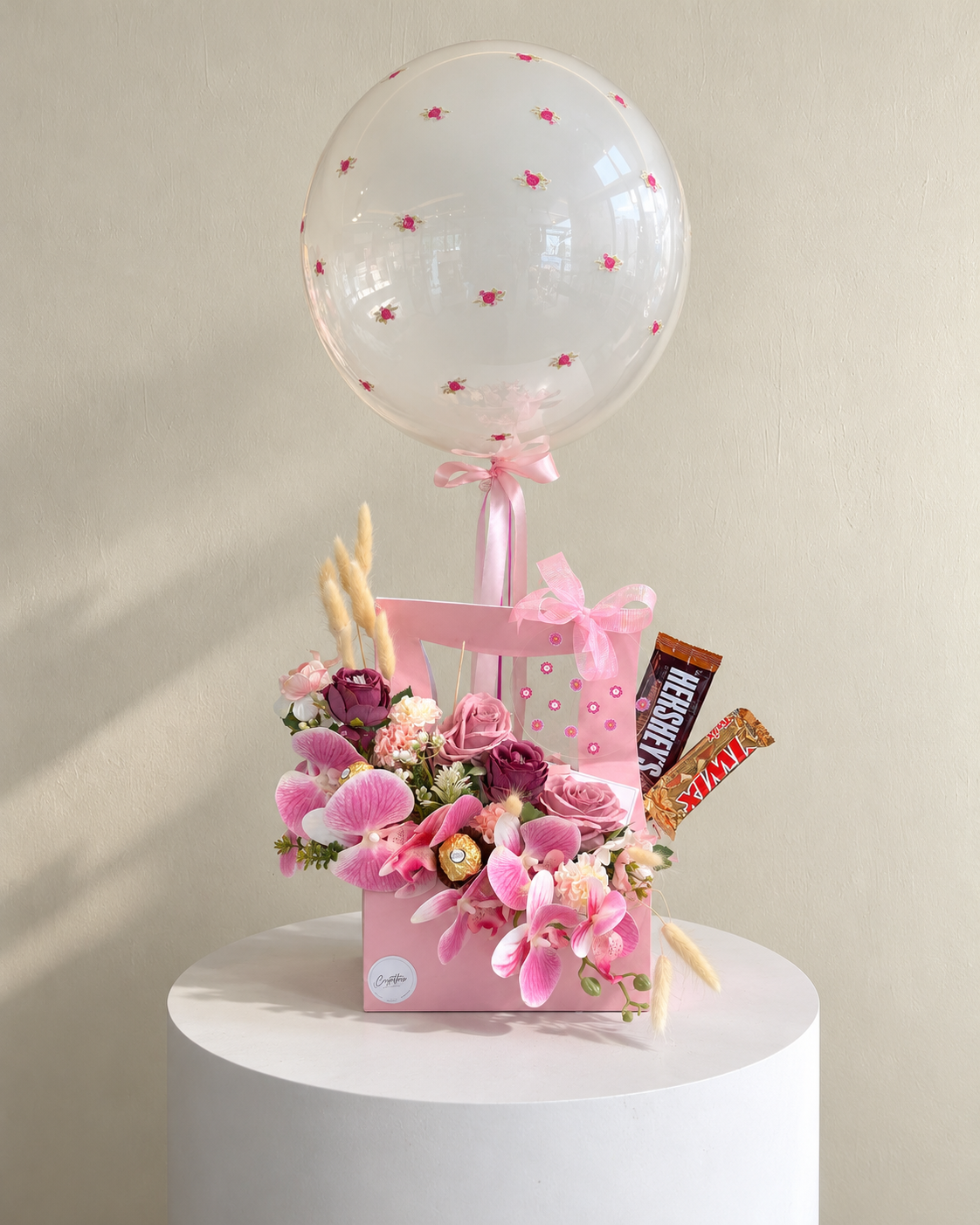 Pink floral gift arrangement with chocolates, a clear floral balloon and pink ribbon.