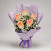 Peach-toned roses and white baby’s breath come together in a delicate bouquet with green foliage. Lavender wrapping and a purple ribbon finish the design for a romantic surprise, birthday greeting or thoughtful thank-you.
