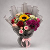 A vibrant mixed bouquet pairing a sunflower with red, pink, peach and ivory roses, purple chrysanthemums and white baby’s breath. Green foliage, layered grey wrapping and a pink ribbon complete an expressive gift for birthdays and special celebrations.