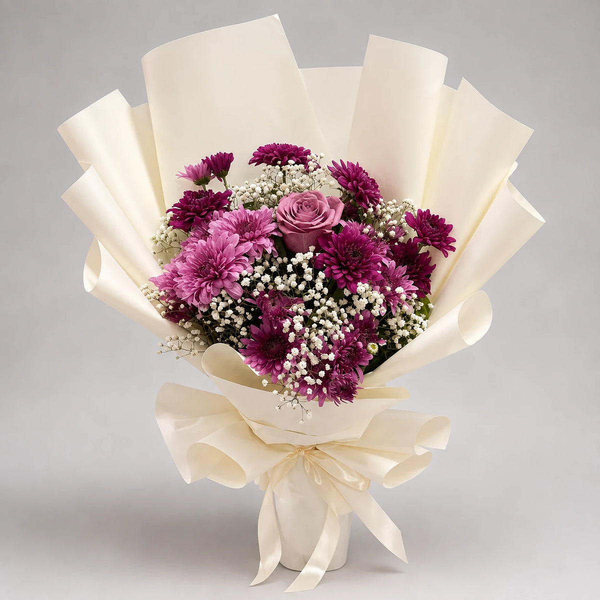 Rich purple and lavender chrysanthemums surround a purple rose, with white baby’s breath and green foliage adding texture. The bouquet is finished in ivory wrapping with a matching ribbon, making a thoughtful gift for birthdays, appreciation and special celebrations.