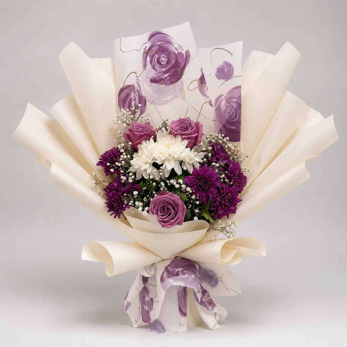 A graceful purple and ivory bouquet combining purple roses, purple and white chrysanthemums, delicate white baby’s breath and greenery. Layered ivory wrapping and a purple floral-print accent create a soft, elegant finish for birthdays, thank-you gifts and thoughtful celebrations.